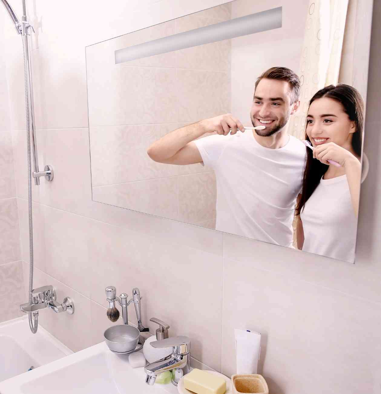 Couple brushing their teeth together in front of a bathroom mirror, promoting daily oral care and healthy smiles.